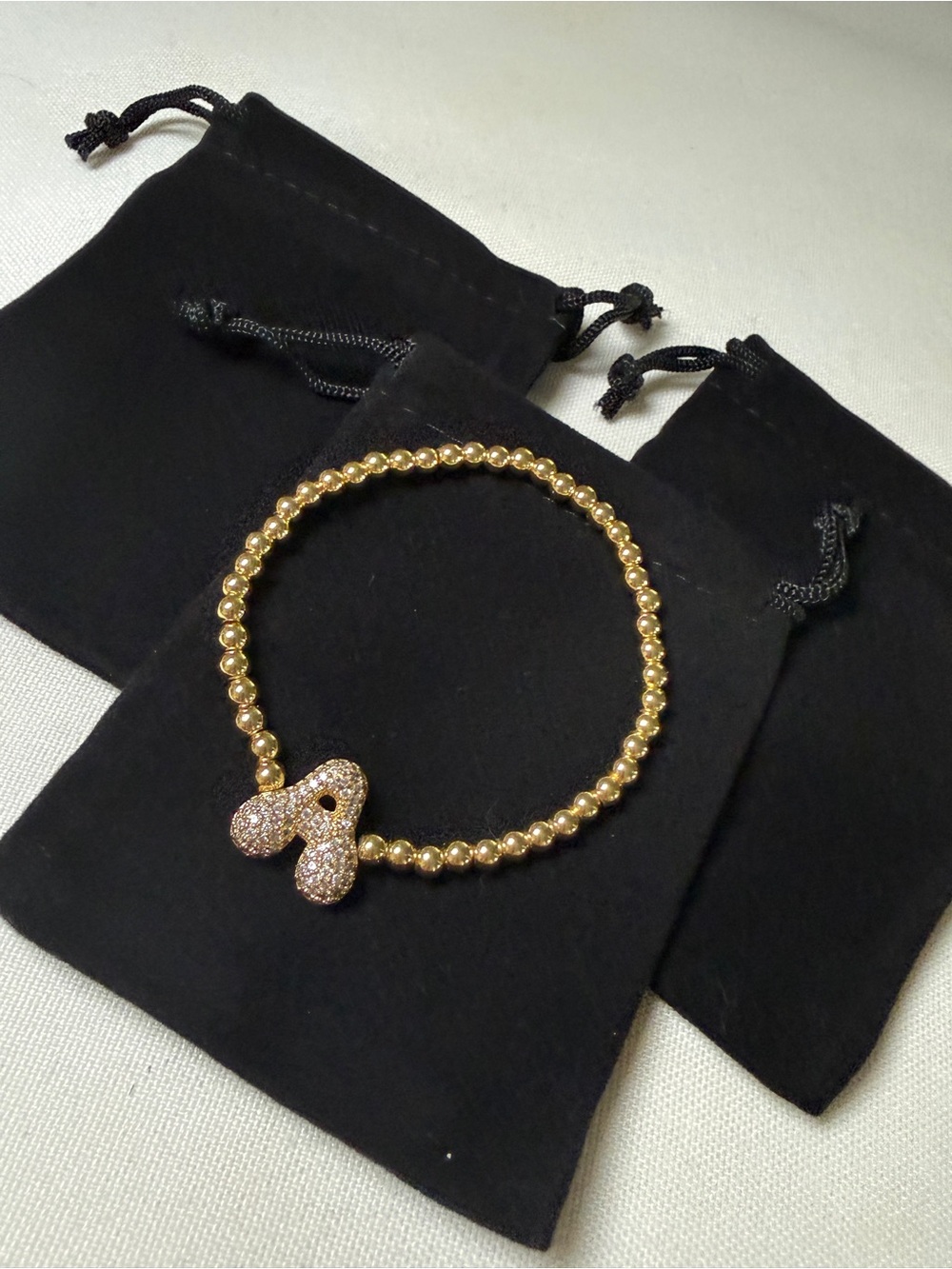gold-tone beaded initial bracelet featuring a sparkly rhinestone letter “A” char